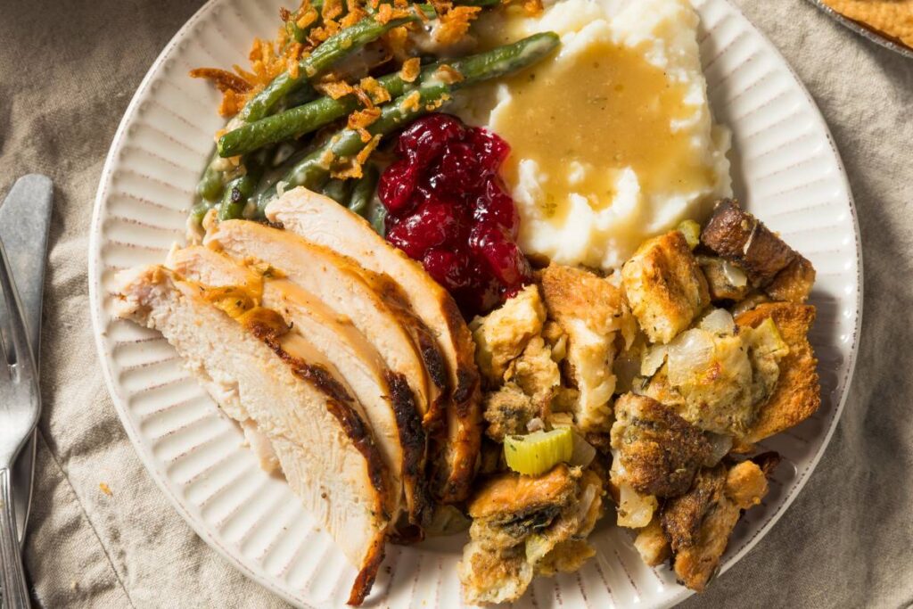 white plate with turkey, mashed potatoes and gravy, stuffing, green bean casserole, and cranberry sauce