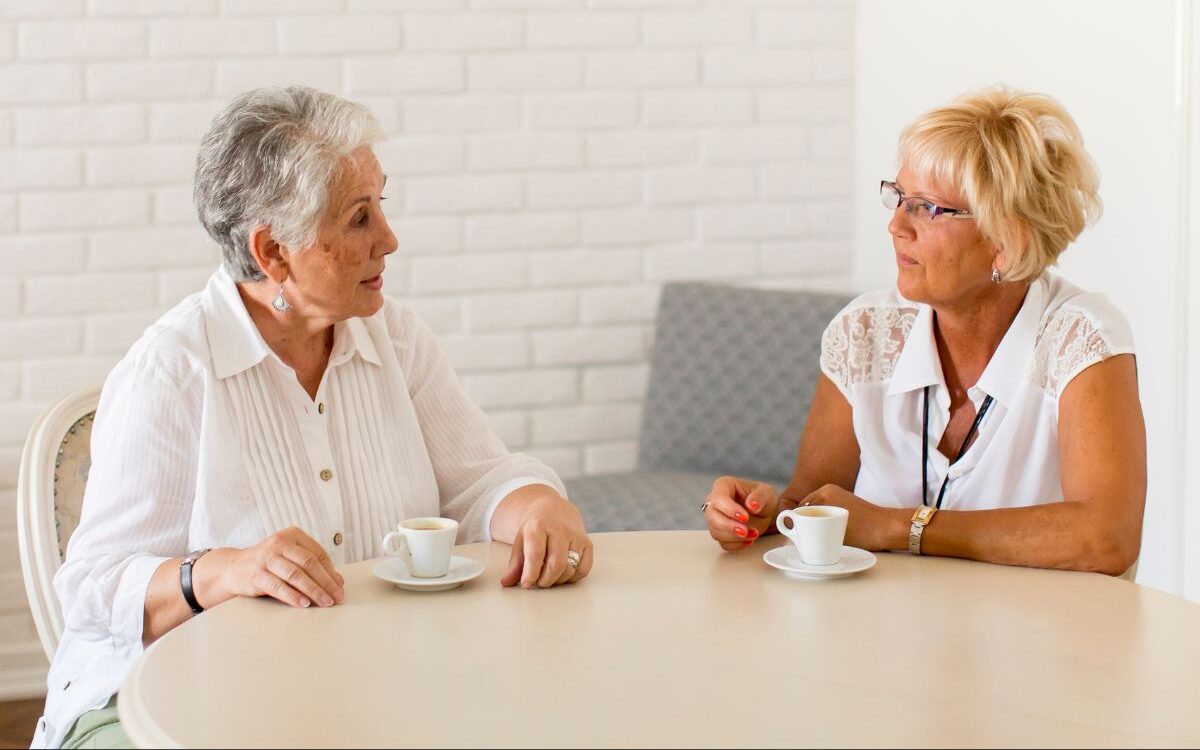 two women sitting at a round table talking while having coffee
