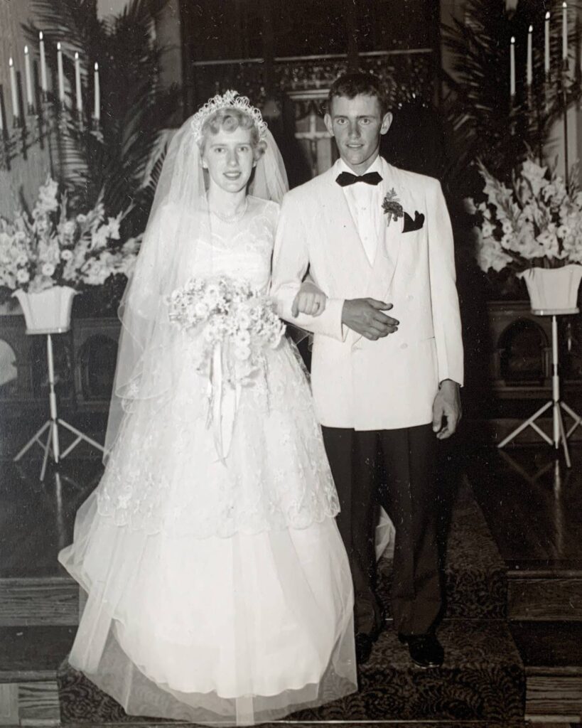 old black and white photo of a bride and groom on their wedding day standing in the front of a church with flowers behind them