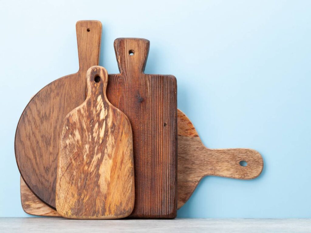 Four wooden charcuterie or cutting boards stacked together and leaned against a blue wall